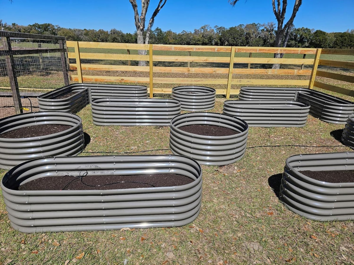 Metal garden beds on a grassy field with a wooden fence in the background 