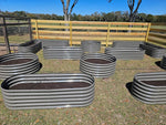 Metal garden beds on a grassy field with a wooden fence in the background 