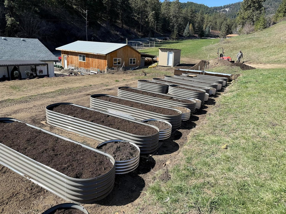 Row of metal garden beds on a farm with buildings and trees in the background 