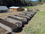 Row of metal garden beds on a farm with buildings and trees in the background 