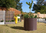 Large brown corrugated metal planter with plants in a garden setting 