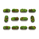 Twelve oval metal herb garden beds arranged in a 3-by-4 grid on a plain white background. Each bed contains assorted green herbs, leafy greens, and small red and orange flowers. 